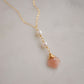 Two white semi-round pearls hang over a natural peach Moonstone faceted drop. The gold style pendant is shown.