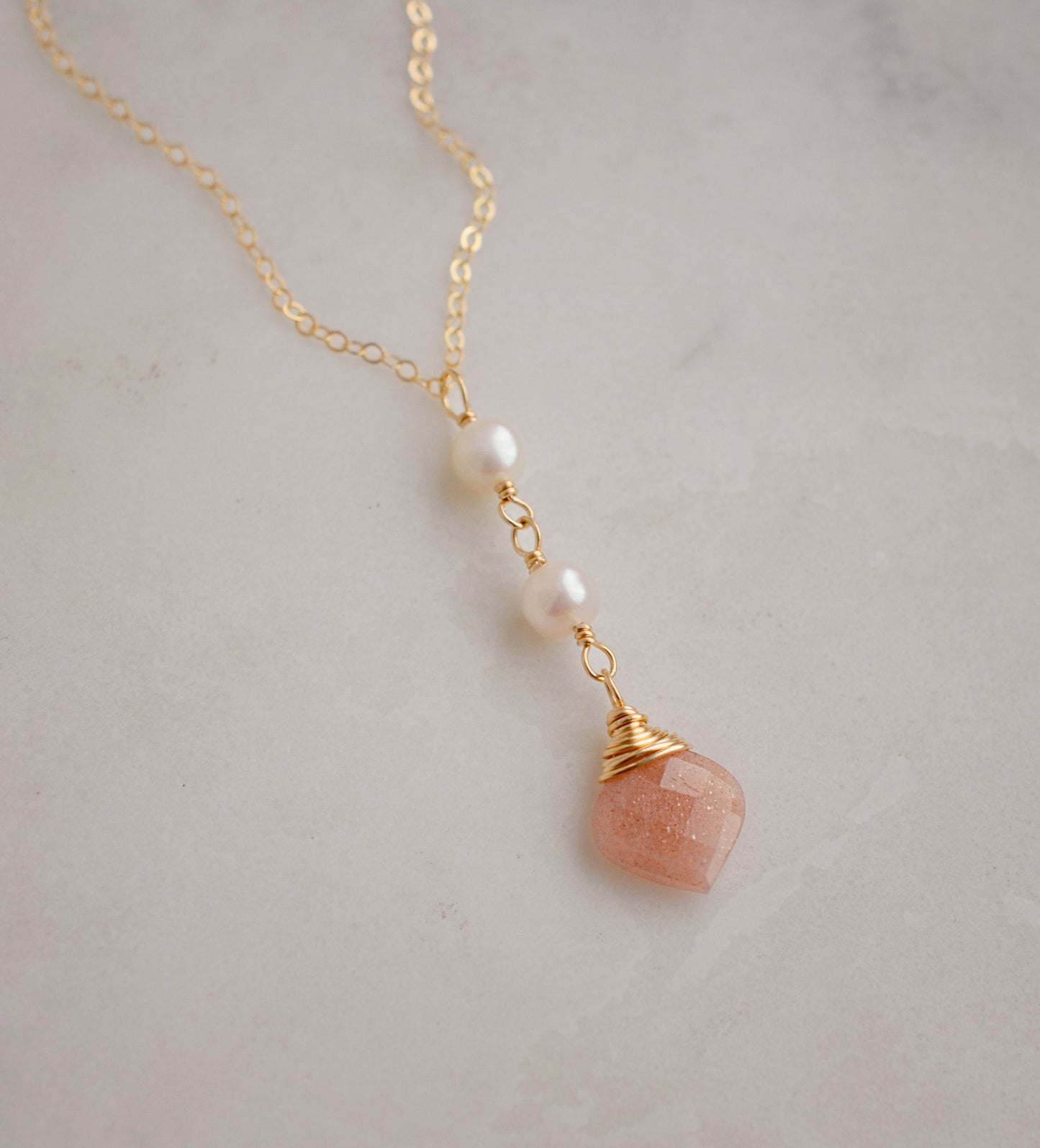 Two white semi-round pearls hang over a natural peach Moonstone faceted drop. The gold style pendant is shown.