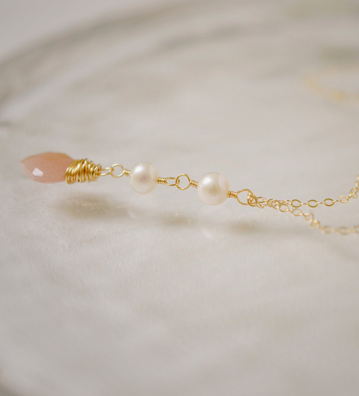 Two white semi-round pearls hang over a natural peach Moonstone faceted drop. The gold style pendant is shown.