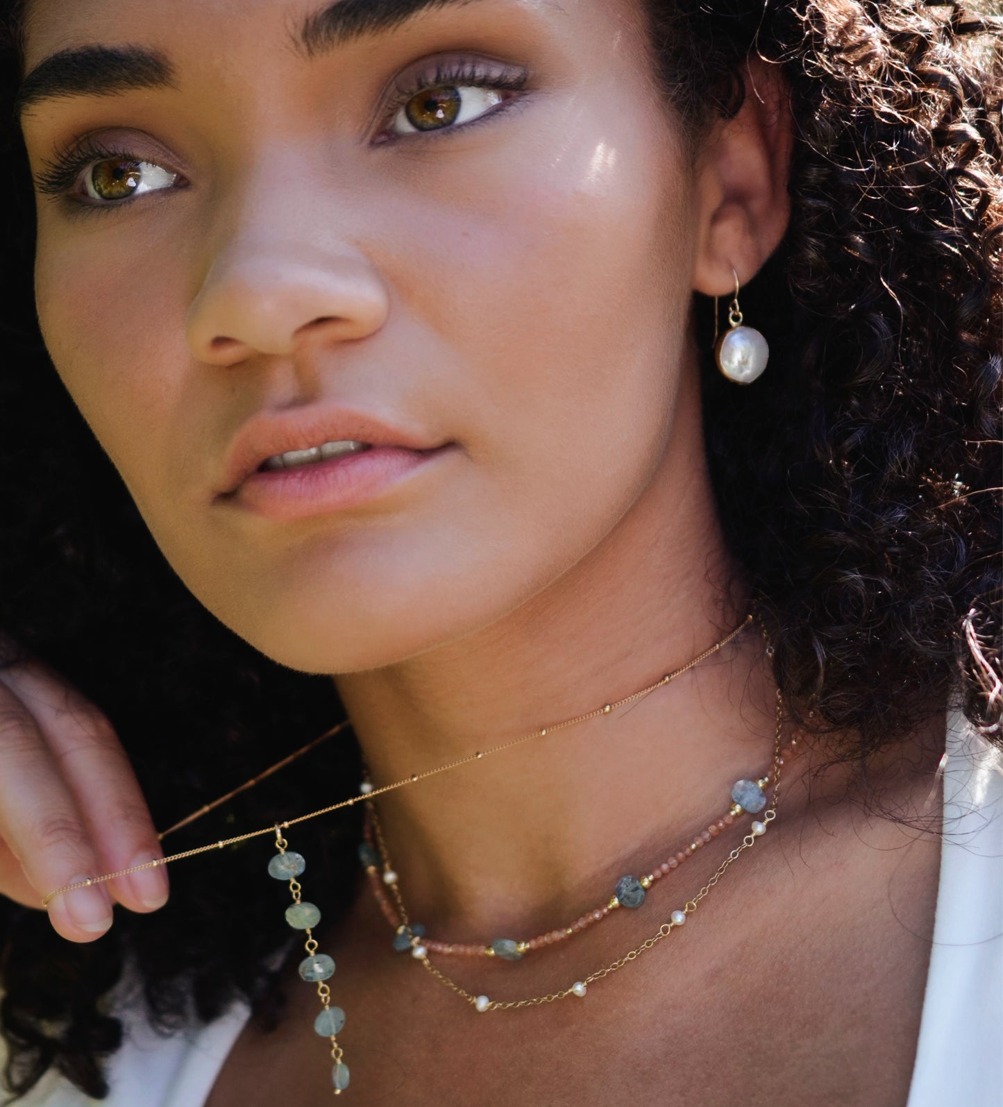 Natural white freshwater pearl dangle earring. The pearl is set in 22k gold electroplate and suspended from 14k gold filled earwires. Modeled image. Also shown, pearl and Kyanite necklace.