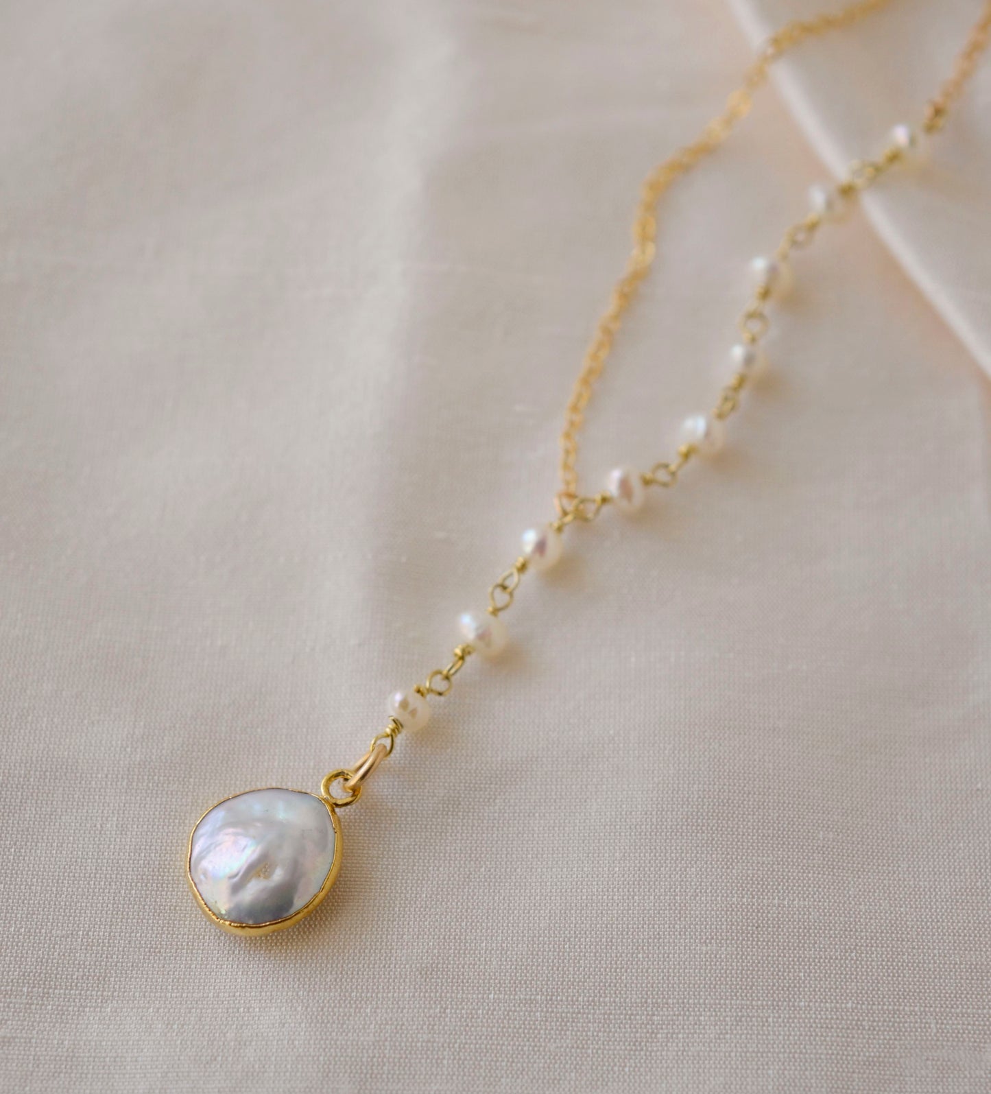 White freshwater pearl necklace with a large coin pearl pendant. Pearls fill one side of the necklace, while the other side is a dainty gold chain.