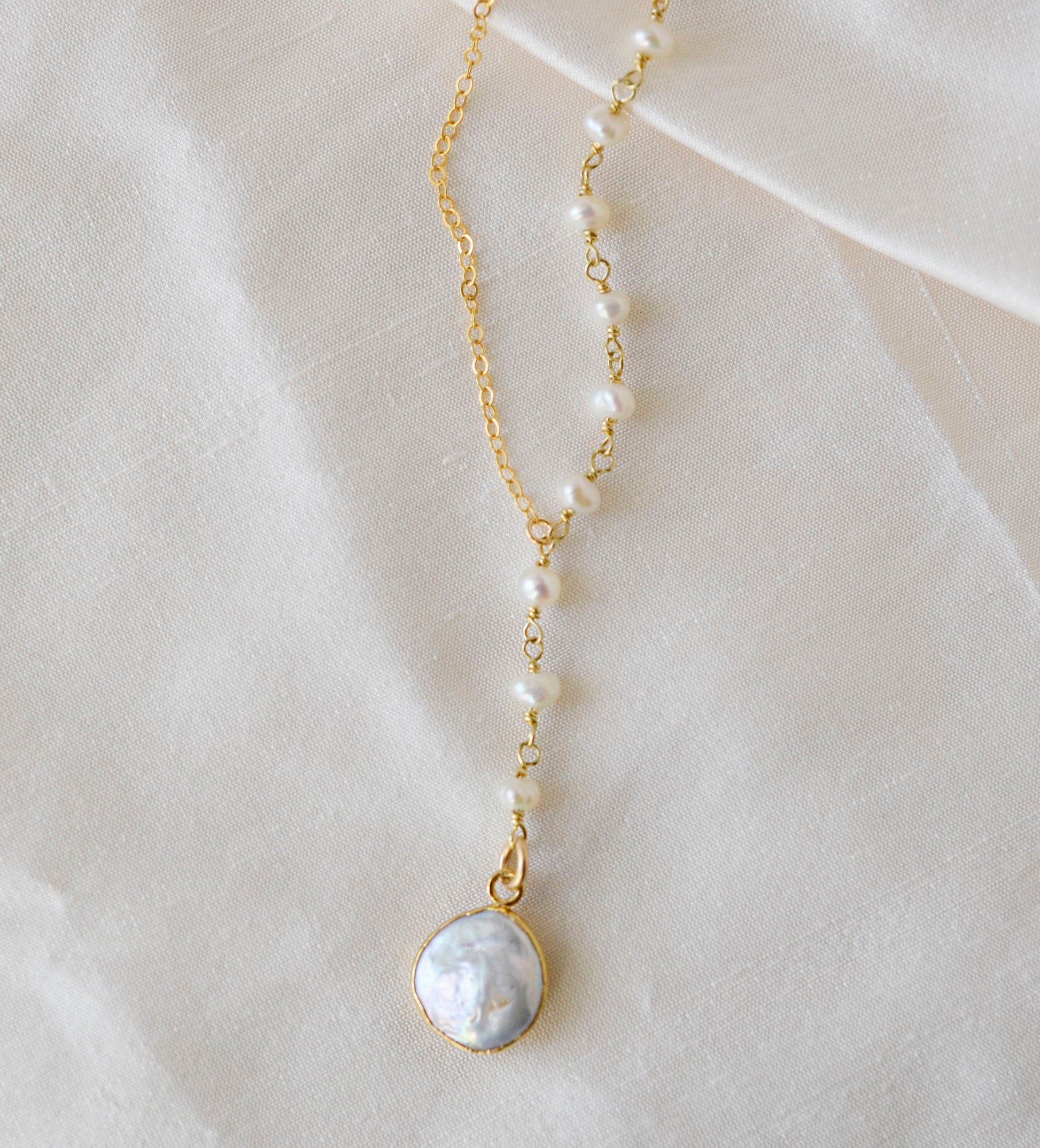 White freshwater pearl necklace with a large coin pearl pendant. Pearls fill one side of the necklace, while the other side is a dainty gold chain.