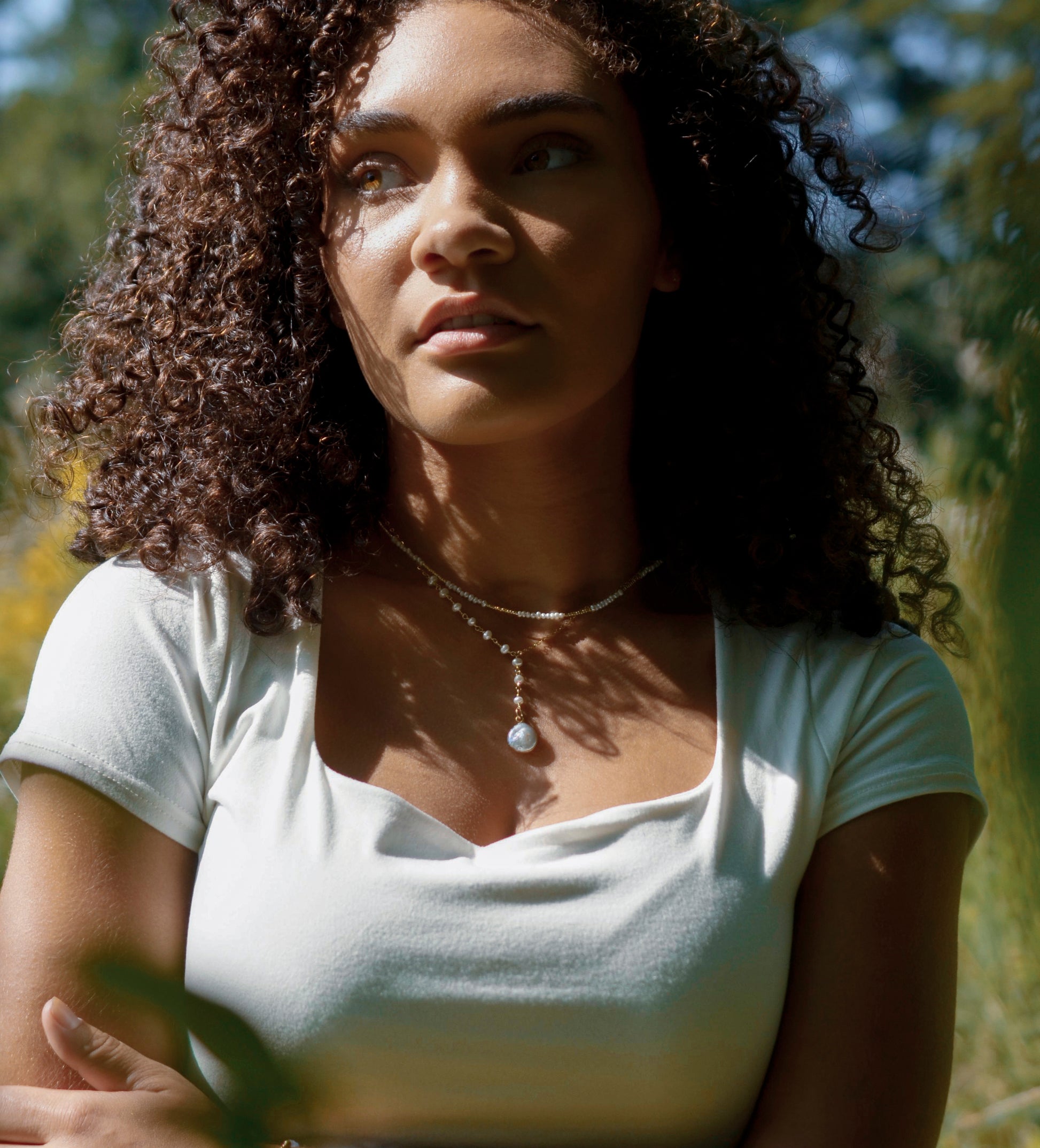 White freshwater pearl necklace with a large coin pearl pendant. Pearls fill one side of the necklace, while the other side is a dainty gold chain. Modeled image.