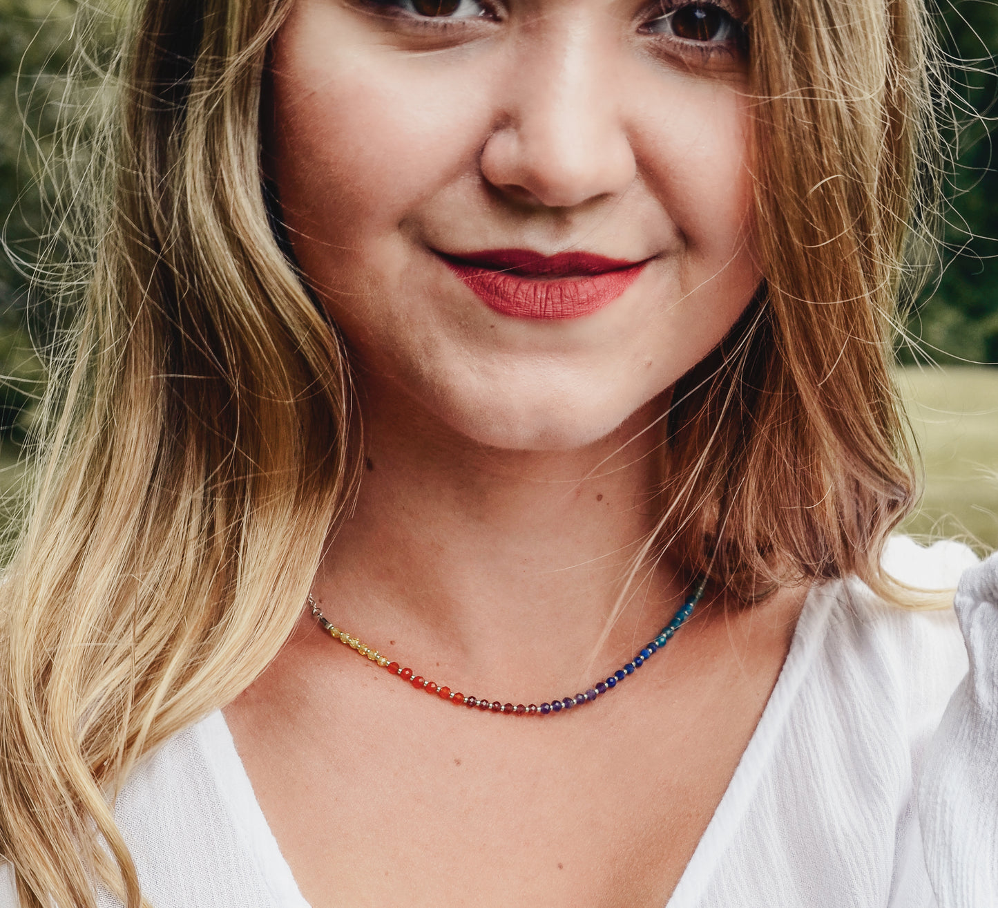 Modeled image. Rainbow chakra gemstone necklace. Crystals are beaded together in this pattern: yellow, orange, red, purple, blue, aqua, green. The silver style is shown.