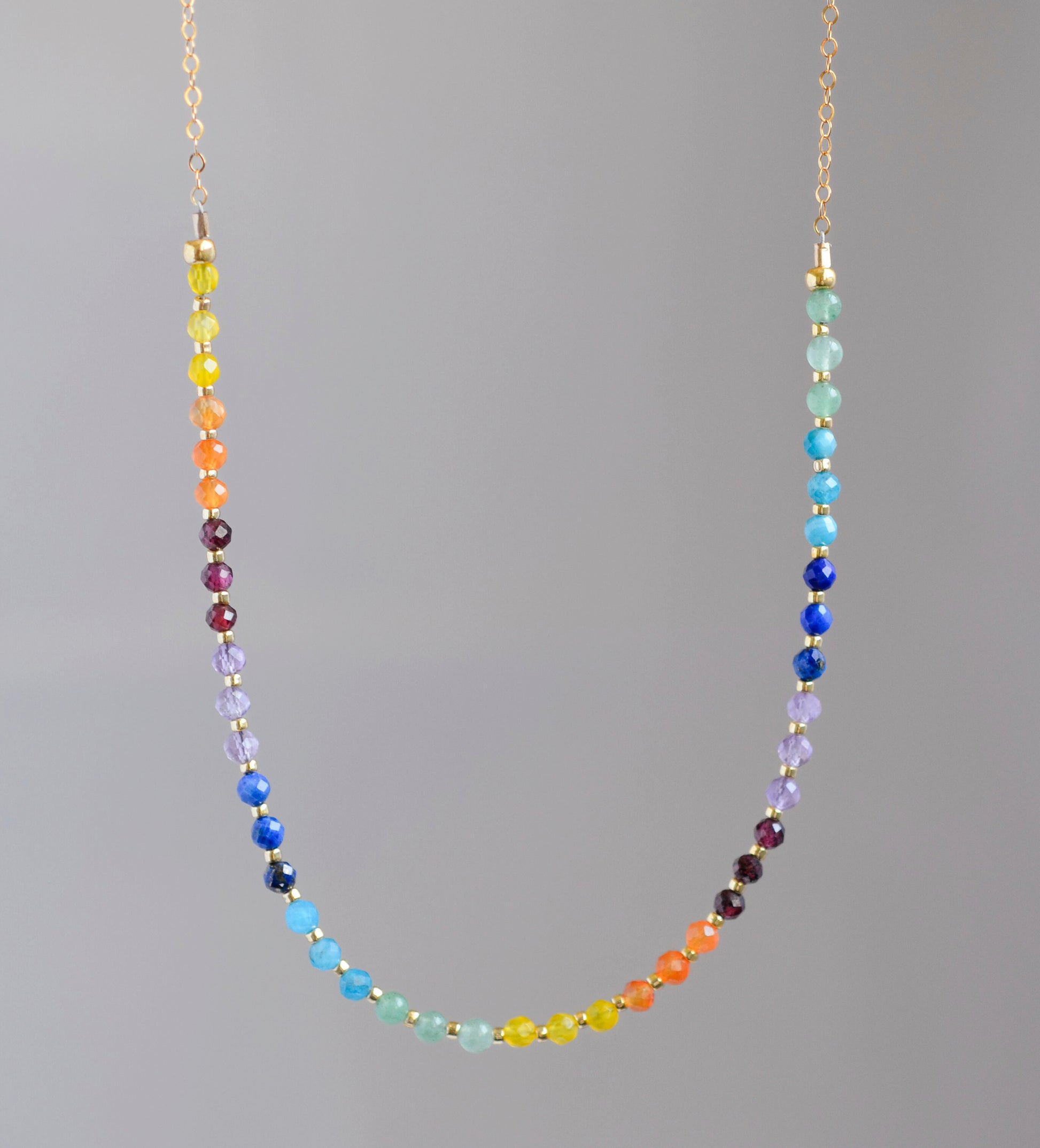 Rainbow chakra gemstone necklace. Crystals are beaded together in this pattern: yellow, orange, red, purple, blue, aqua, green. The gold style is shown.