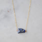 Raw blue lapis lazuli stone suspended from a gold chain.