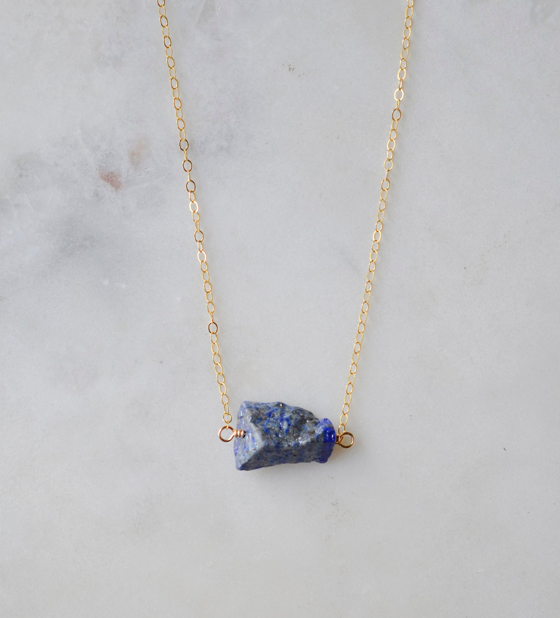 Raw blue lapis lazuli stone suspended from a gold chain.