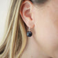 Natural smooth polished coin shape black Shungite dangle from sterling silver earring hooks. Modeled image. 