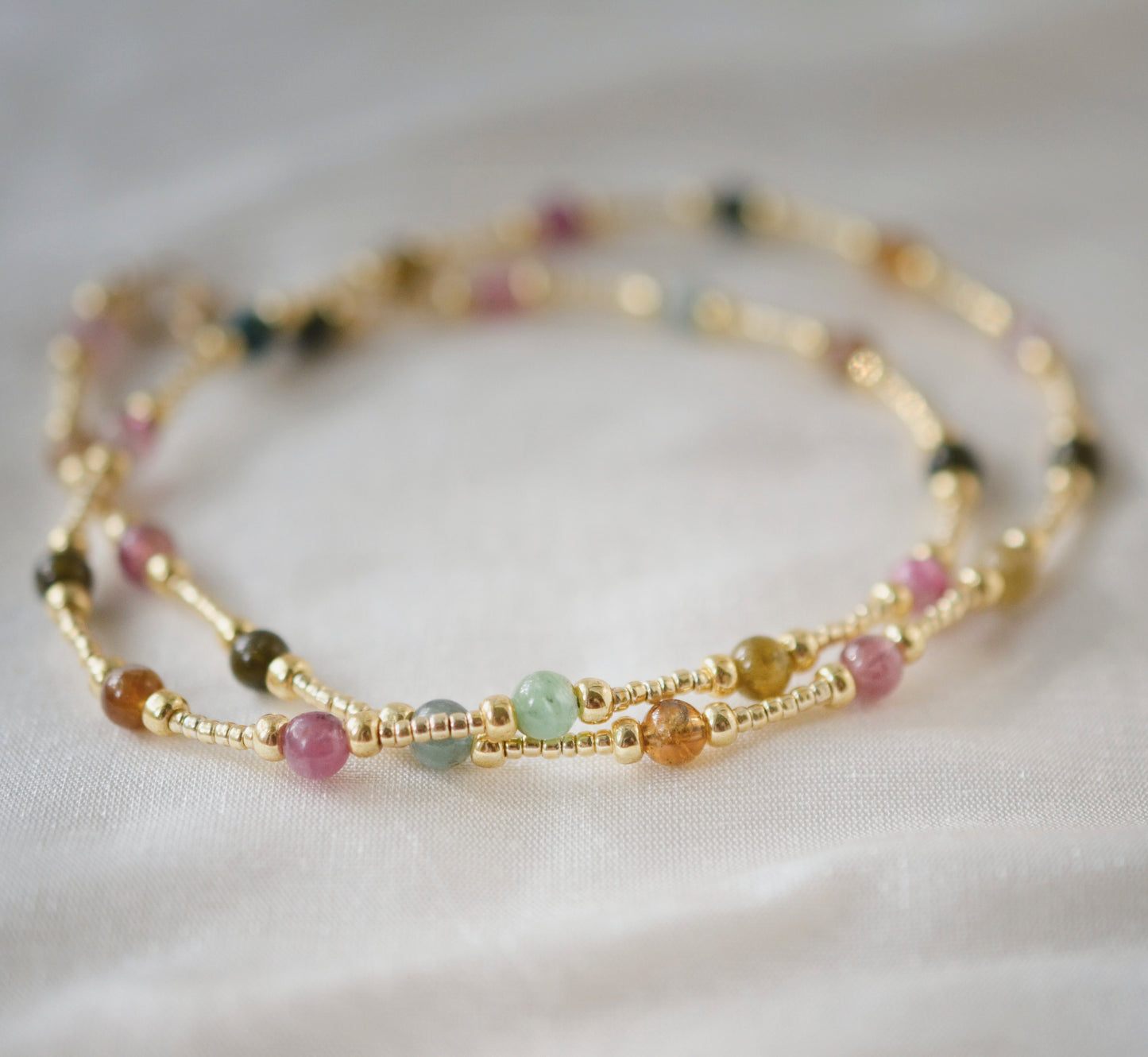 Multicolored, smooth polished Tourmaline gems hand-beaded with gold plated glass beads. Colors range from pink, green, brown, yellow, or black.