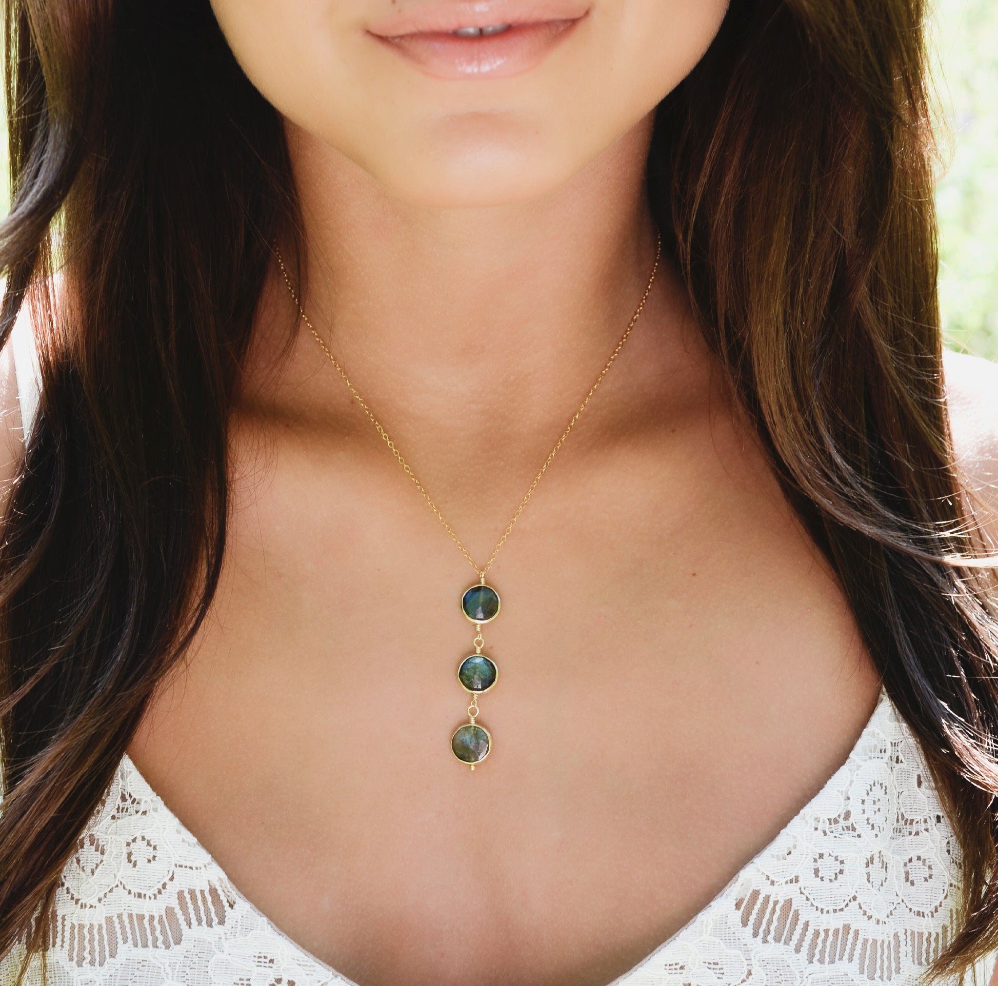 Woman wearing a gold necklace with three natural blue and green circle shaped labradorite gemstones suspended from a 14k gold filled chain. This handmade necklace is also available in sterling silver. 