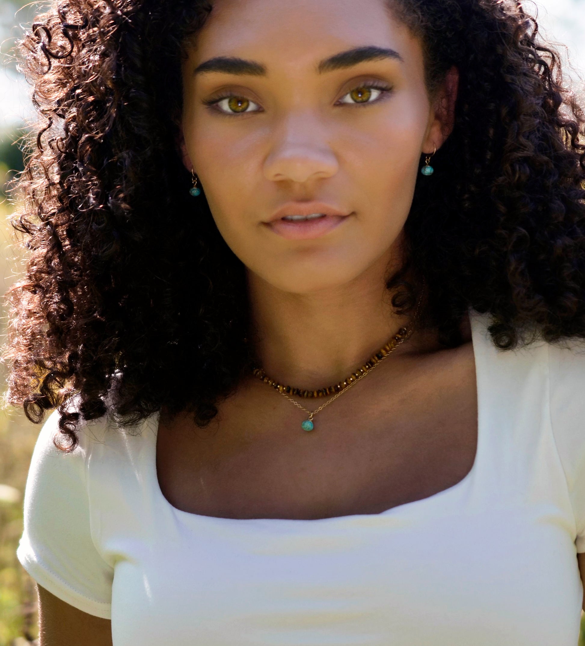 Small round turquoise faceted drops suspended from gold filled earwires. Each stone has a different matrix with light to dark brown coloring. Modeled image. Shown with matching necklace and Tiger Eye Necklace.