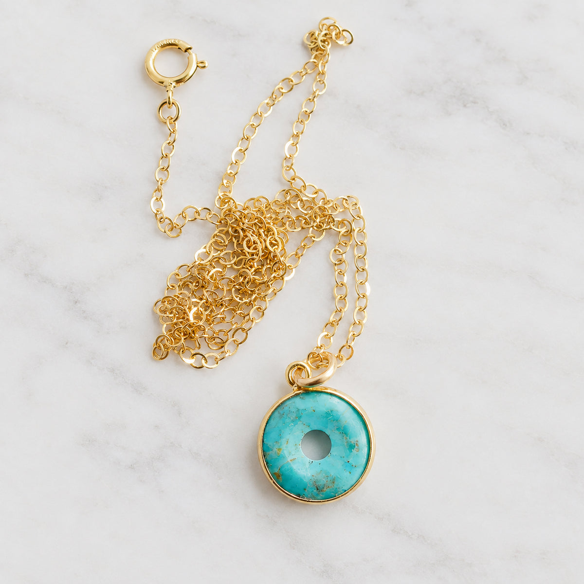 A closeup image of a gold turquoise necklace with a pendant that's a donut shape. Wear as an infinity necklace. Handmade in Connecticut and also available in sterling silver. 
