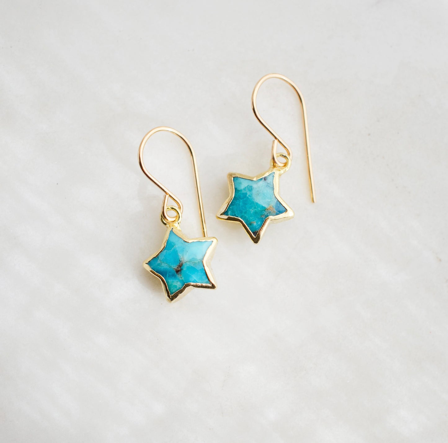 Star-shaped earrings with turquoise stones set in gold. These earrings are handmade by Gemnia Jewelry in Connecticut.