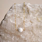 A natural white howlite necklace on a crystal quartz background. The stone is round with natural gray marbling and set on a 14k gold filled chain. Also available in sterling silver. 