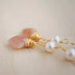 Two white semi-round pearls hang over natural peach Moonstone faceted drops. The gold style is shown.