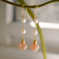 Two white semi-round pearls hang over natural peach Moonstone faceted drops. The gold style is shown.