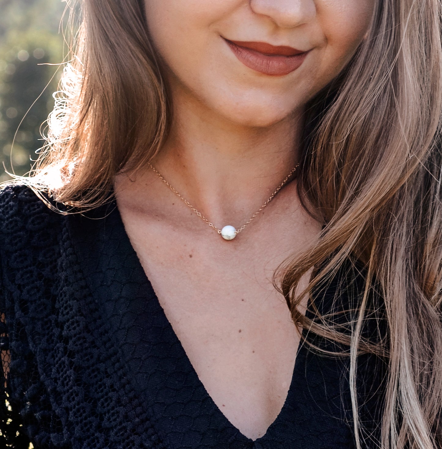 A woman is wearing a natural white howlite necklace. The stone is round with natural gray marbling and set on a 14k gold filled chain. Also available in sterling silver. 