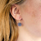 Purple-pink raw ruby stones suspended from sterling silver earwires. The stones are rough and in their natural hexagonal shape. Modeled image.