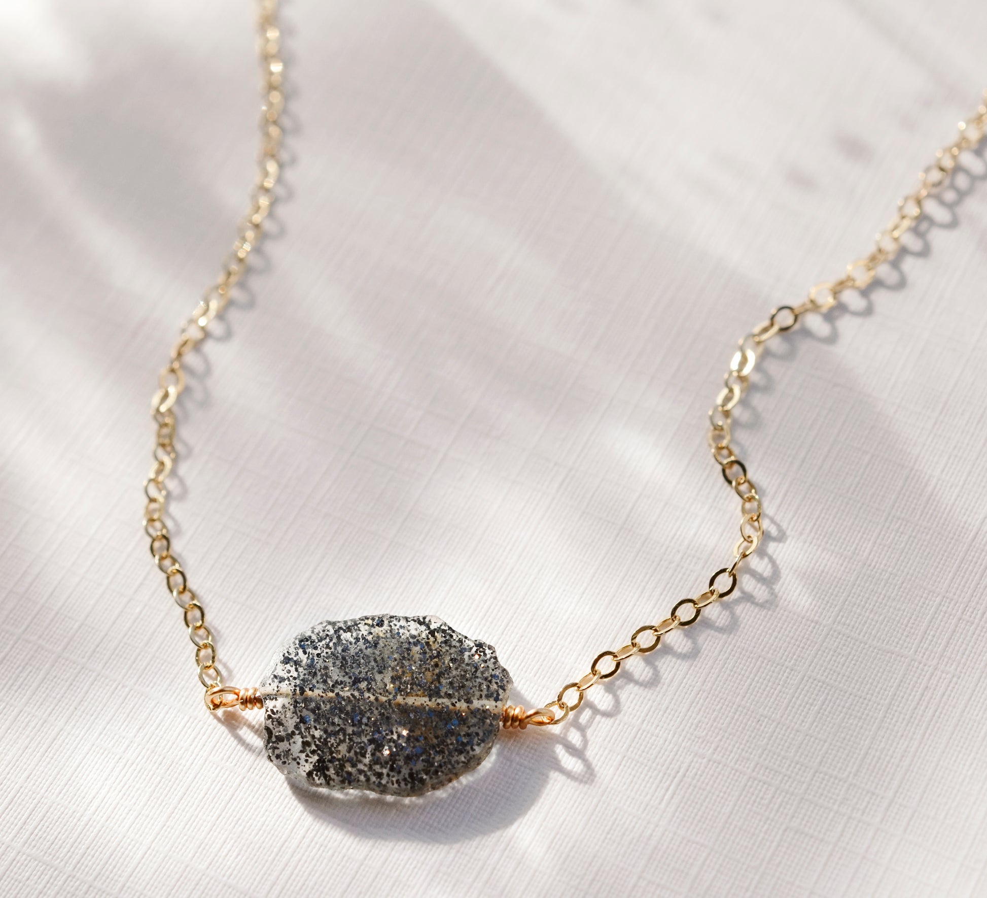 Close up of a natural black sunstone slice with rough edges set onto a gold filled cable chain.