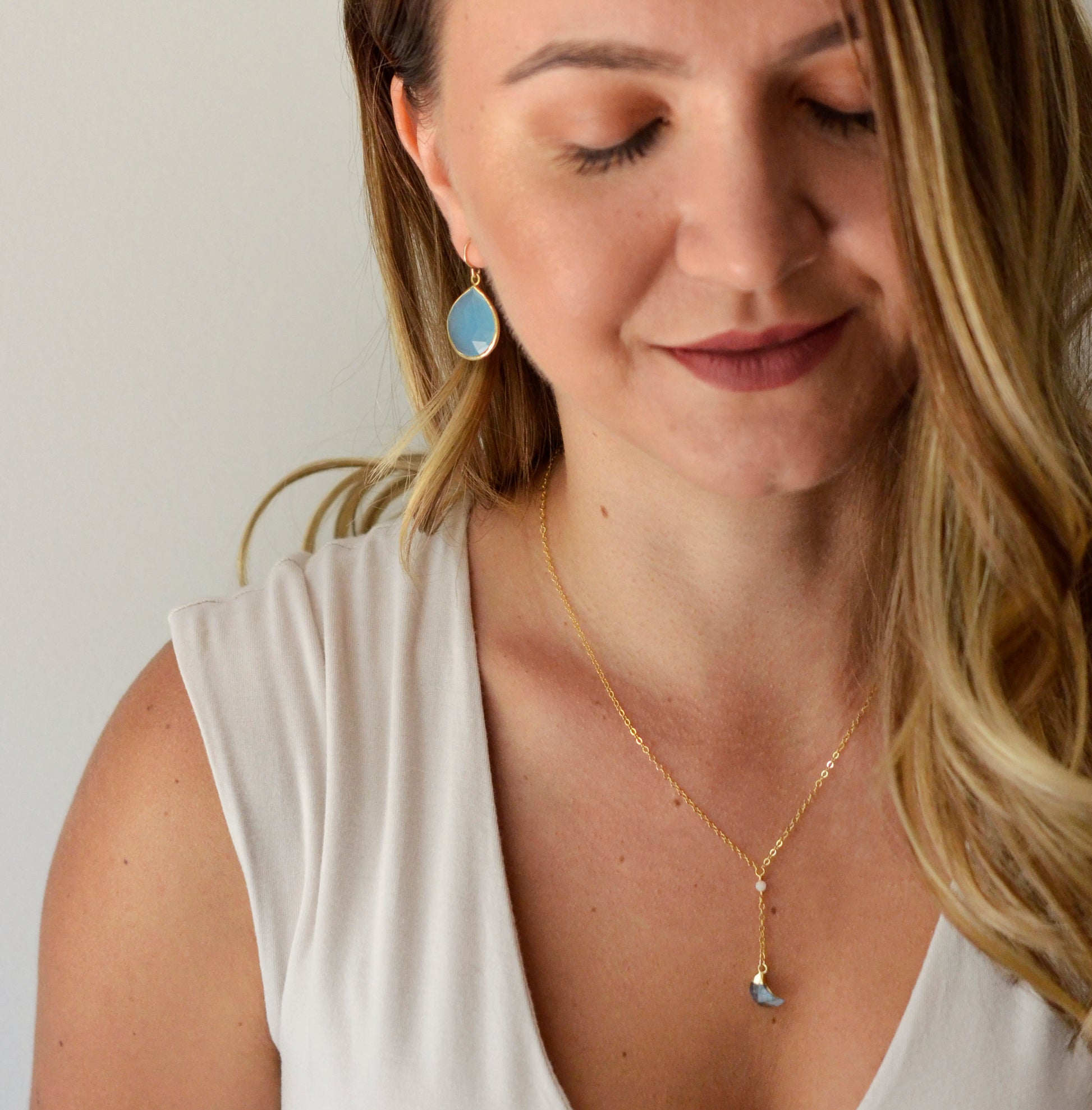 Large blue chalcedony teardrop gemstones bezeled in gold and suspended from earwires. Modeled image. Shown with a crescent moon pendant.