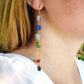 Long gemstone earrings made with a rainbow of raw gemstones. Colors include: purple, blue, aqua, green, yellow, orange, and red. Modeled image. 