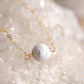 Close up image. A natural white howlite necklace on a crystal quartz background. The stone is round with natural gray marbling and set on a 14k gold filled chain. Also available in sterling silver. 
