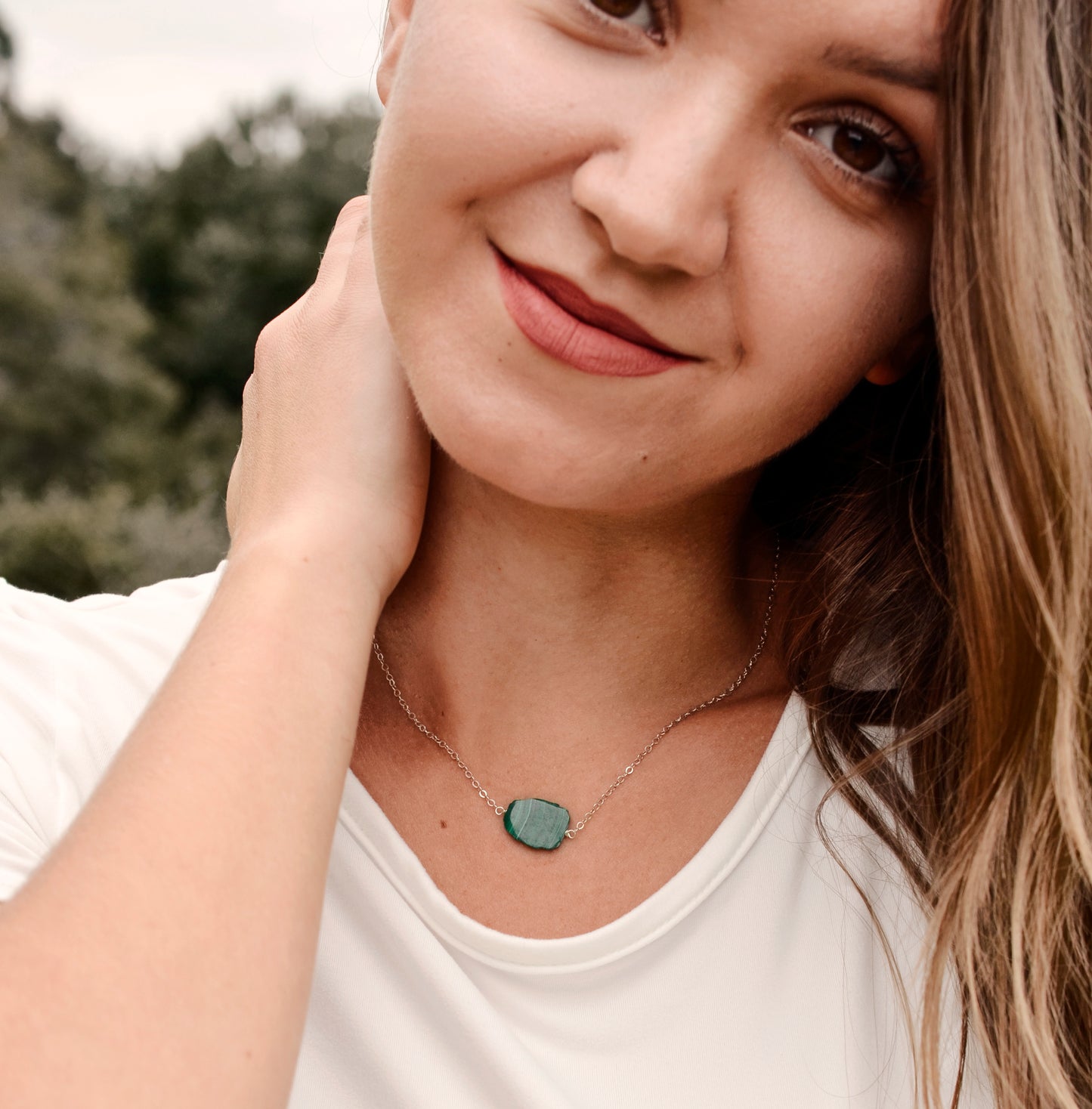 Natural green Malachite smooth polished slice with raw edges. Each stone is an irregular oval shape and has a variety of banding. Shown on a sterling silver chain. Modeled image.