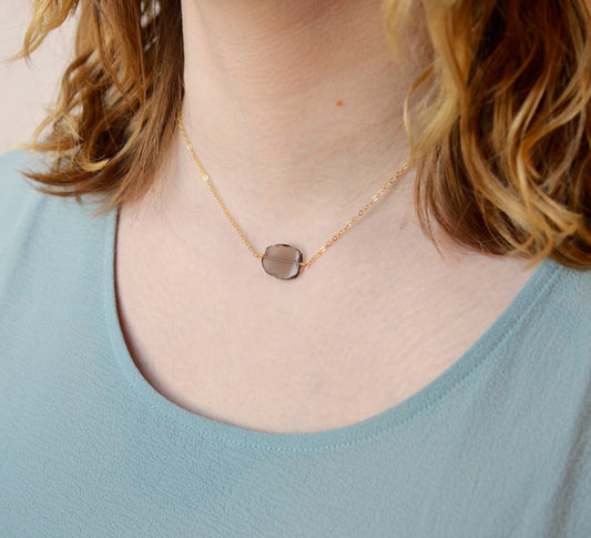 An irregular oval shape, smooth polished Smokey Quartz stone set onto a 14k gold filled chain. The stones edges are raw and irregular. Modeled image.